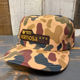 Camo 5-panel workhorse hat made of durable fabric sits on a wooden surface, designed for versatile outdoor use.