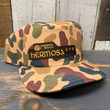 Camo 5-panel work hat with patch and snapback closure, displayed on wooden surface.