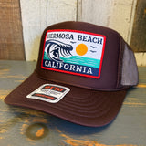 Brown high-crown trucker hat with mesh back, featuring a colorful patch of wave, sun, and birds. Suitable for casual wear.