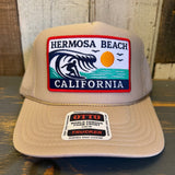 Khaki trucker hat with foam front panel featuring sun, wave, and surfer patch; casual style suitable for everyday wear.