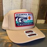 Khaki trucker hat with surfer, wave, sun, and seagulls patch; mesh back; casual beachwear accessory.