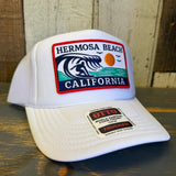 White high crown trucker hat with mesh back, featuring a patch of a wave, sun, and bird.