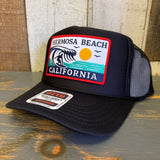 Black high-crown trucker hat with mesh back, featuring a wave, sun, and ocean patch on the front.