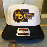Black and natural 5-panel mid-profile cap made of fabric, displayed on a wooden surface. Suitable for casual wear.