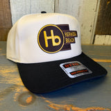 Black and natural 5 panel mid profile cap with logo, displayed on a wooden surface. For casual or outdoor wear.