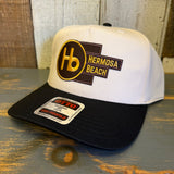 Black and natural 5-panel mid-profile cap with a fabric front, displayed on a wooden surface. Suitable for everyday wear.