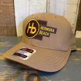 Wheat brown 5-panel mid-profile cap with Hb logo, displayed on a rustic wooden surface; casual everyday headwear.
