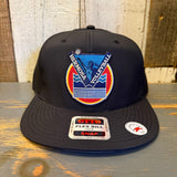 Black 6-panel snapback hat with volleyball patch, displayed on a wooden surface.