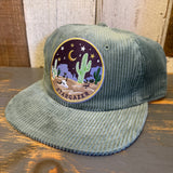 Sage corduroy hat with desert scene patch showing cacti and stars; suitable for casual wear.