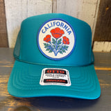 Jade green high crown trucker hat with mesh back, displayed on a wooden surface.