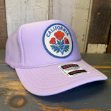 Lavender trucker hat with orange poppy patch, mesh back, cotton front, displayed on a wooden surface.