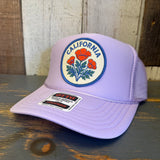 Lavender California poppy trucker hat with mesh panels displayed on a wooden surface.