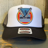 Black and white vintage volleyball trucker hat with mesh back, displayed on a wooden surface.