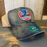 Blue denim and khaki trucker cap with Hermosa Vista patch, displayed on a wooden surface.