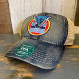 Blue denim and khaki trucker cap with a volleyball patch and green Legacy sticker, ideal for casual or sports use.