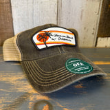 A retro-style six-panel trucker cap with sunset design sits on a wooden surface, featuring mesh panels and adjustable snapback.