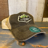 Black and khaki trucker cap with mesh back on a rustic wooden surface, suitable for casual or outdoor use.