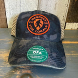 Six-panel trucker cap in navy field camo and java, features a recycled visor, suitable for everyday outdoor wear.