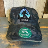 Navy and brown camo six-panel trucker cap with mesh back and green eco sticker, suitable for casual outdoor wear.