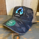 Six-panel trucker cap in navy field camo and java colors, mesh back, set on a wooden surface.