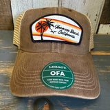 Brown and khaki six-panel trucker cap with retro sunset patch and green sticker, suitable for casual wear.
