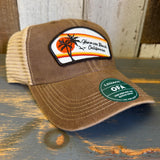 Brown and khaki trucker cap with patch, mesh back, and Zeroline OFA sticker resting on wooden surface.