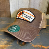 Brown/khaki retro sunset trucker cap with mesh back, shown on rustic wood surface. Ideal for casual outdoor wear.