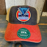 A black and white mesh trucker cap with volleyball text sits on a wooden table, suitable for casual outdoor wear.