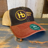 Six-panel trucker cap in black, cardinal, and khaki with mesh back rests on a wooden surface.