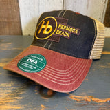 Six-panel trucker cap in black, cardinal, and khaki with mesh back and green Legacy sticker on the brim.