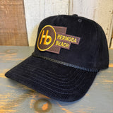 Black corduroy baseball cap with yellow patch displayed on a wooden surface.