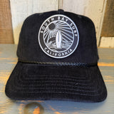 Black corduroy baseball cap with surf patch showing sun, waves, and board; suitable for casual outdoor wear.