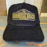 Black corduroy baseball cap with embroidered text, displayed on a wooden surface.