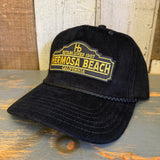 Black corduroy cap with yellow patch, displayed on rustic wooden surface.