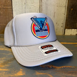 Grey mesh trucker hat with fabric patch and OTTO sticker displayed on a wooden surface.