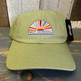 Desert green 6-panel cotton dad hat with sunburst patch, displayed on a wooden surface.