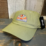 Desert green dad hat with sunrise patch, cotton material, displayed on a wooden surface. Suitable for casual wear.