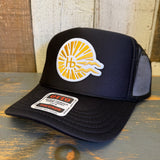 Black mesh trucker hat with classic logo, resting on wood; ideal for outdoor or beach use.