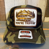 Camo trucker hat with mesh back and front patch showing a van, trees, and mountains. Suitable for casual outdoor wear.