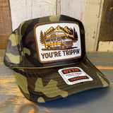 Camo trucker hat with mesh back, front patch depicting a camper van and mountains; casual outdoor wear.