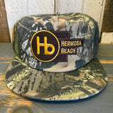 Camo 5-panel snapback hat with gold Hb patch and adjustable closure, suitable for everyday casual wear.