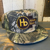 5-panel surf camo hat with logo patch and adjustable strap, featuring green and brown tones. Suitable for casual outdoor wear.