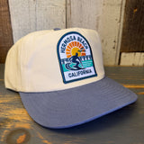 Slate blue and natural workhorse hat with embroidered patch featuring surfer, sunset, and pier; durable casual wear.