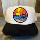 Two-tone snapback hat, black and natural, with a sunset pier patch; casual wear, adjustable fit.