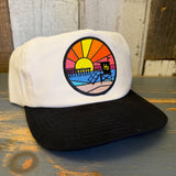 Two-tone hat with front patch featuring sunset, pier, and lifeguard tower. Casual use; typical beachwear style.