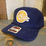 Navy blue corduroy baseball cap with sunburst logo, displayed on a wooden surface.