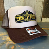 Brown and khaki trucker hat with yellow embroidered text on the front, mesh back, and adjustable strap.