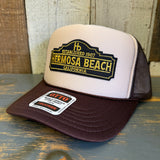 Brown and khaki trucker hat with mesh back, displayed on rustic wooden surface.