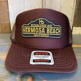 Brown high-crown trucker hat with mesh back and yellow embroidered text. Suitable for casual wear.