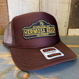 Brown high crown trucker hat with yellow patch and mesh back, suitable for casual wear.